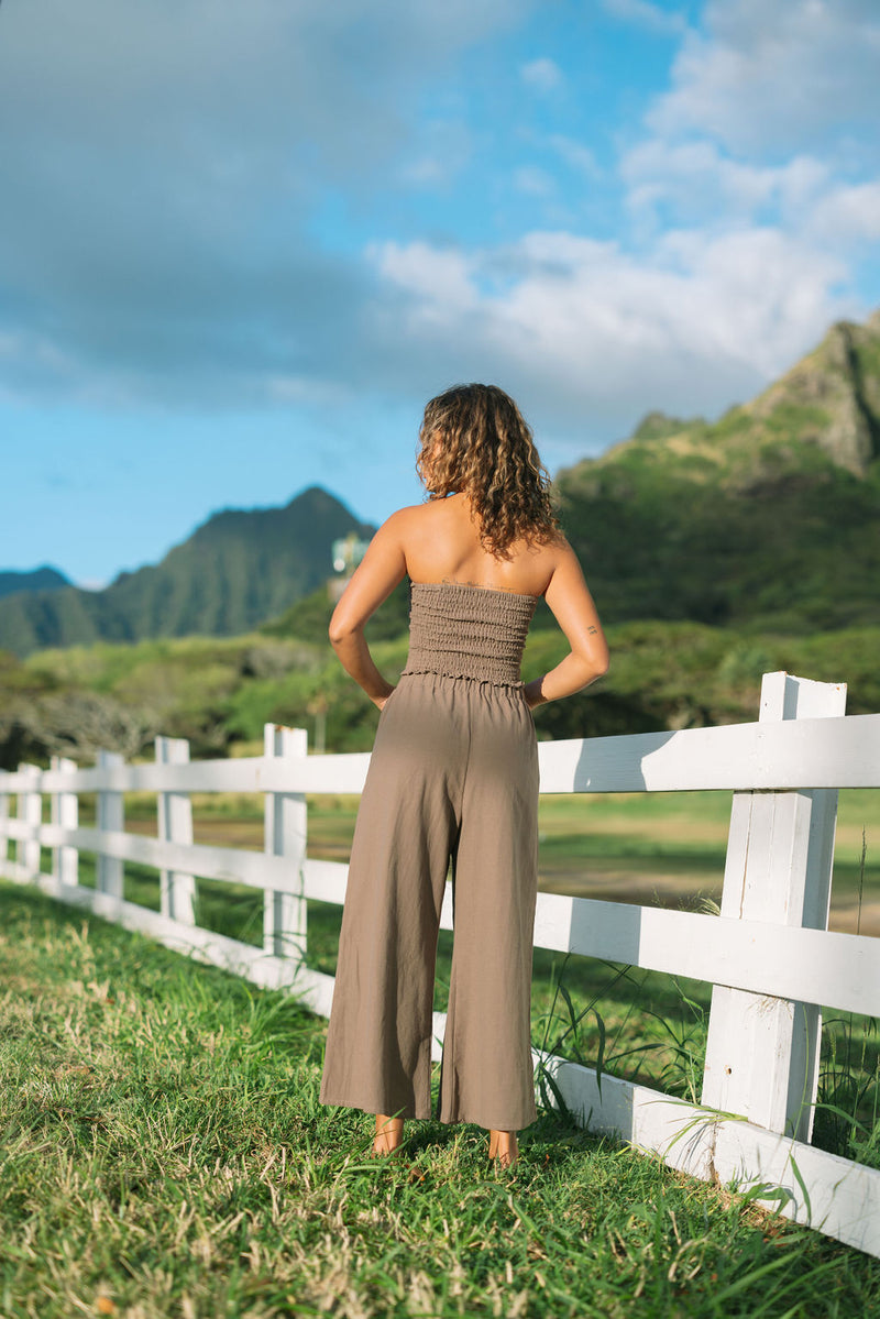 Woman wearing smocked tube top and loose pant in medium brown linen.