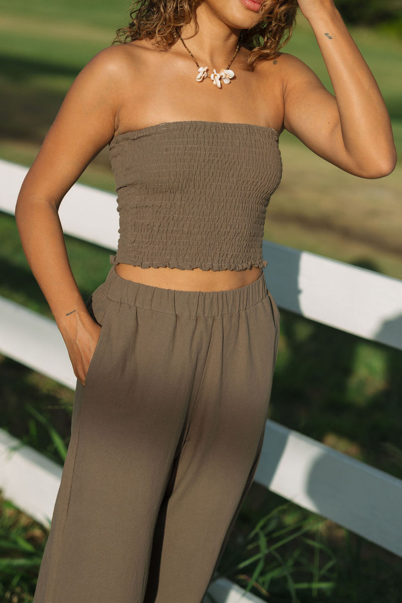 Woman wearing smocked tube top and pant in medium brown linen.