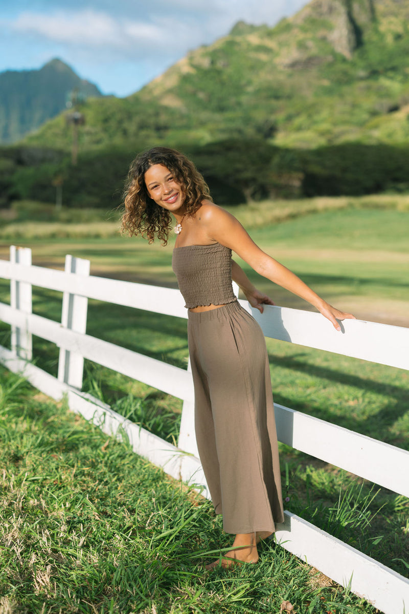 Woman wearing smocked tube top and loose pant in medium brown linen.