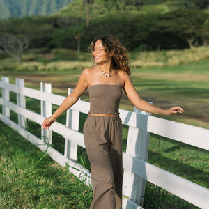 Woman wearing smocked tube top and loose pant in medium brown linen.