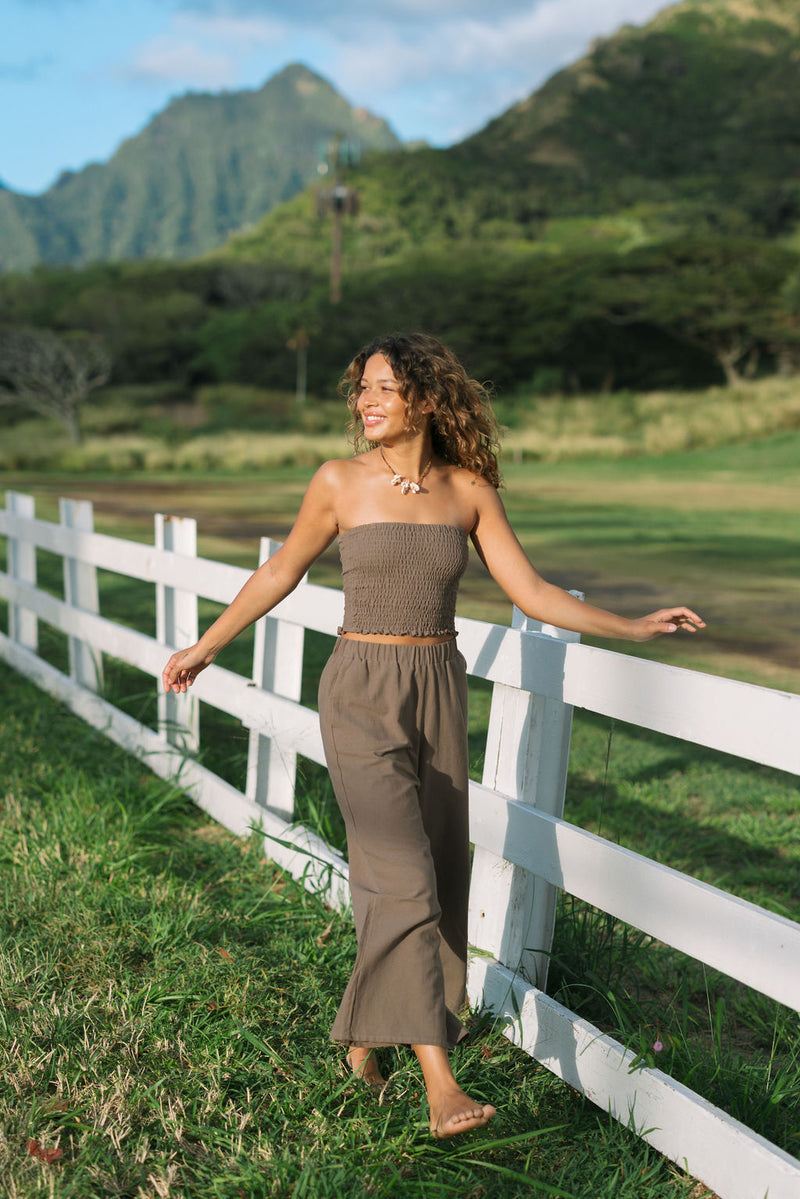 Woman wearing smocked tube top and loose pant in medium brown linen.