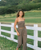 Woman wearing smocked tube top and loose pant in medium brown linen.