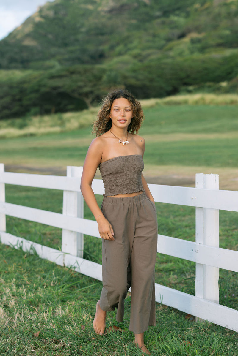 Woman wearing smocked tube top and loose pant in medium brown linen.