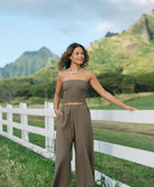 Woman wearing smocked tube top and loose pant in medium brown linen.