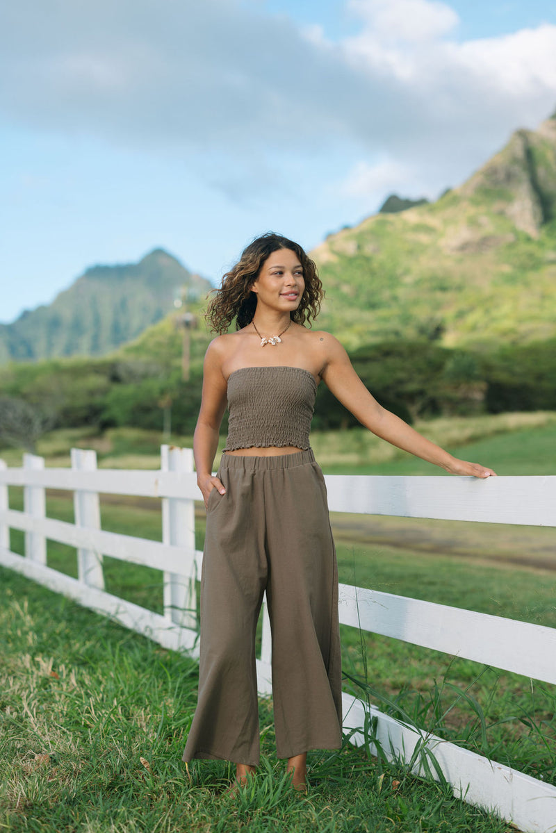 Woman wearing smocked tube top and loose pant in medium brown linen.