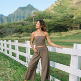 Woman wearing smocked tube top and loose pant in medium brown linen.