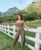 Woman wearing smocked tube top and loose pant in medium brown linen.