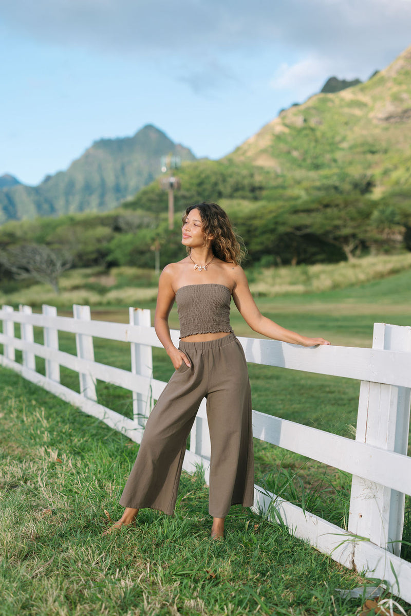 Woman wearing smocked tube top and loose pant in medium brown linen.