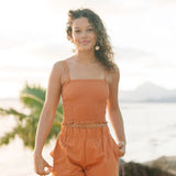 Woman wearing burnt orange linen smocked tube top with spaghetti straps and short.