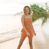 Woman wearing burnt orange linen smocked tube top with spaghetti straps and short.