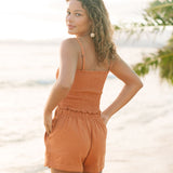 Woman wearing burnt orange linen smocked tube top with spaghetti straps and short.