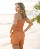 Woman wearing burnt orange linen smocked tube top with spaghetti straps and short.