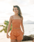 Woman wearing burnt orange linen smocked tube top with spaghetti straps and short.