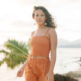 Woman wearing burnt orange linen smocked tube top with spaghetti straps and short.