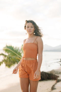 Woman wearing burnt orange linen smocked tube top with spaghetti straps and short.