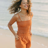Woman wearing burnt orange linen smocked tube top with spaghetti straps and short.