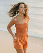 Woman wearing burnt orange linen smocked tube top with spaghetti straps and short.