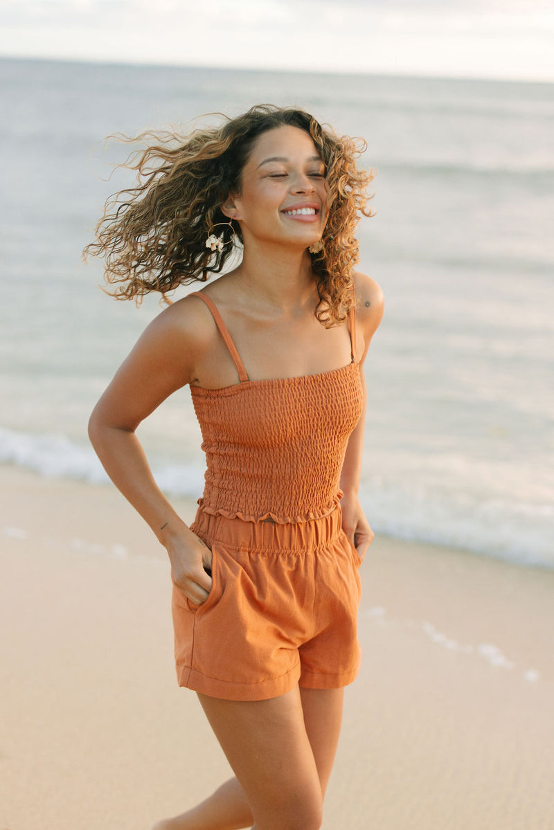 Woman wearing burnt orange linen smocked tube top with spaghetti straps and short.