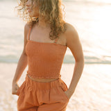 Woman wearing burnt orange linen smocked tube top with spaghetti straps and short.