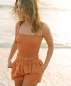 Woman wearing burnt orange linen smocked tube top with spaghetti straps and short.