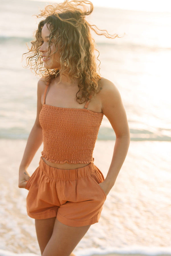 Woman wearing burnt orange linen smocked tube top with spaghetti straps and short.