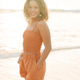 Woman wearing burnt orange linen smocked tube top with spaghetti straps and short.