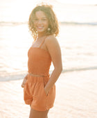 Woman wearing burnt orange linen smocked tube top with spaghetti straps and short.