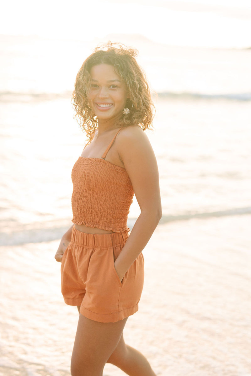 Woman wearing burnt orange linen smocked tube top with spaghetti straps and short.