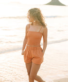 Woman wearing burnt orange linen smocked tube top with spaghetti straps and short.