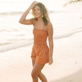 Woman wearing burnt orange linen smocked tube top with spaghetti straps and short.