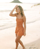 Woman wearing burnt orange linen smocked tube top with spaghetti straps and short.