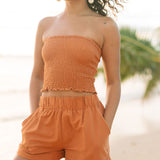 Woman wearing burnt orange linen smocked tube top and short.