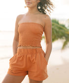 Woman wearing burnt orange linen smocked tube top and short.