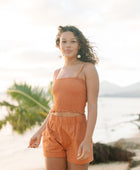 Woman wearing burnt orange linen smocked tube top with spaghetti straps and short.