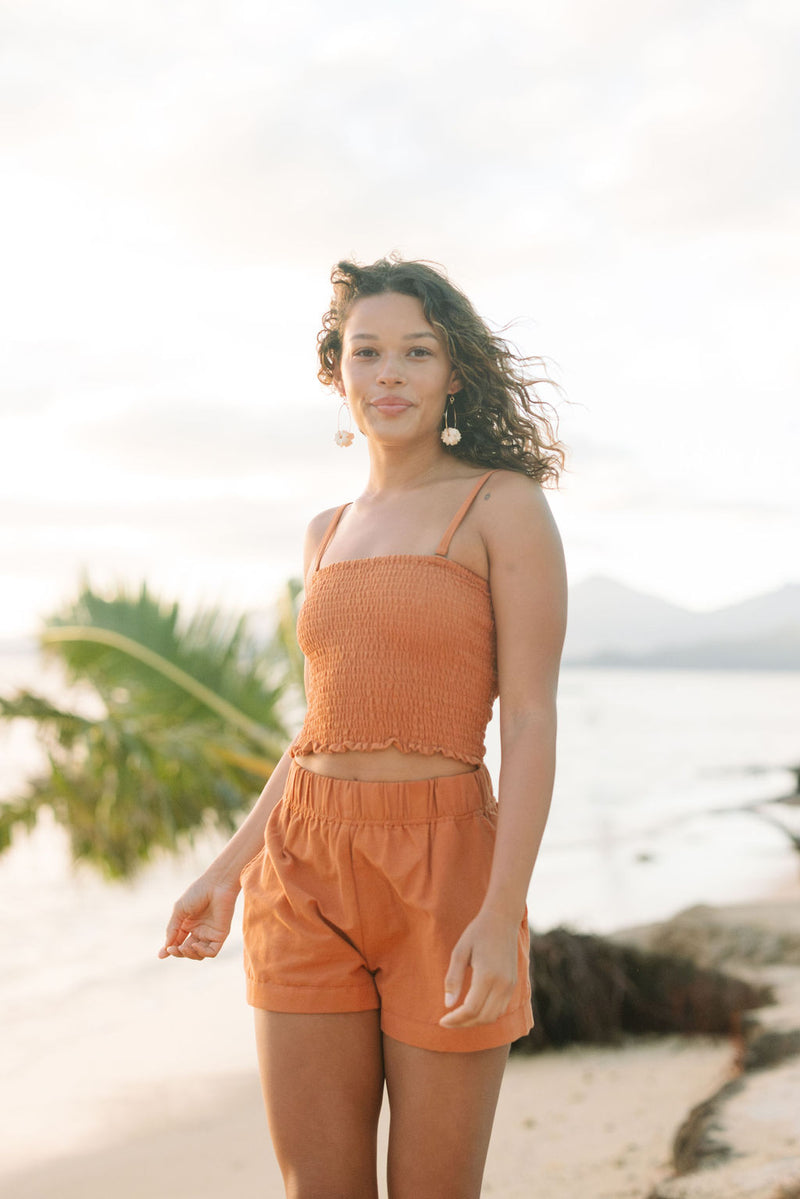 Woman wearing burnt orange linen smocked tube top with spaghetti straps and short.