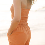 Woman wearing burnt orange linen smocked tube top and short.