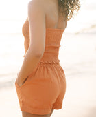 Woman wearing burnt orange linen smocked tube top and short.