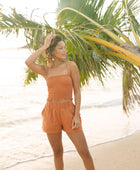 Woman wearing burnt orange linen smocked tube top and short.