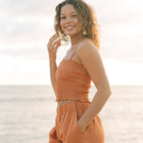 Woman wearing burnt orange linen smocked tube top with spaghetti straps and short.