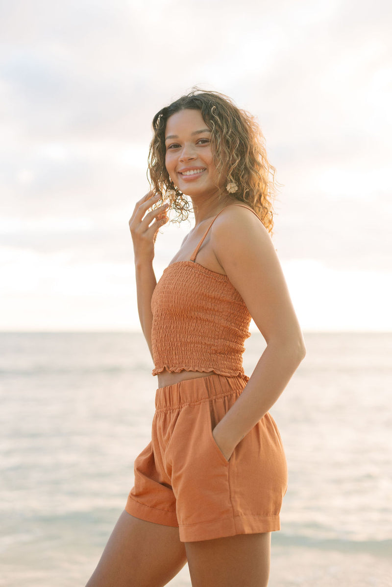 Woman wearing burnt orange linen smocked tube top with spaghetti straps and short.