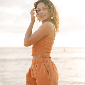 Woman wearing burnt orange linen smocked tube top with spaghetti straps and short.