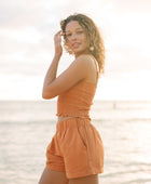 Woman wearing burnt orange linen smocked tube top with spaghetti straps and short.