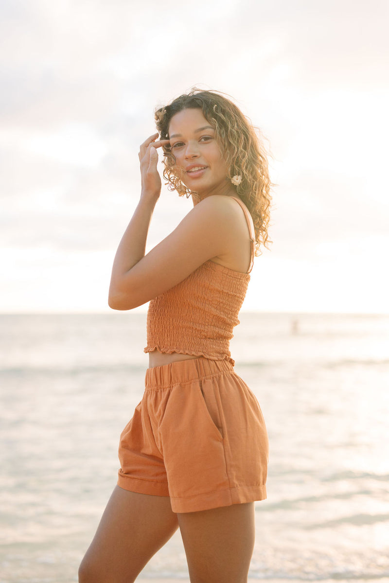 Woman wearing burnt orange linen smocked tube top with spaghetti straps and short.