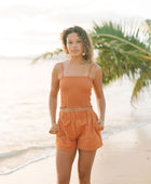 Woman wearing burnt orange linen smocked tube top with spaghetti straps and short.