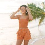 Woman wearing burnt orange linen smocked tube top with spaghetti straps and short.