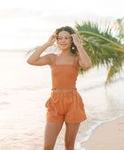 Woman wearing burnt orange linen smocked tube top with spaghetti straps and short.