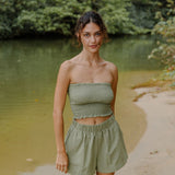 Woman wearing smocked tube top and short in medium green linen.