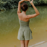 Woman wearing smocked tube top and short in medium green linen.