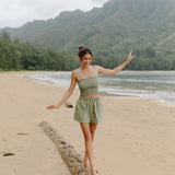 Woman wearing smocked tube top with spaghetti straps and short in medium green linen.