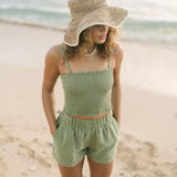 Woman wearing smocked tube top with spaghetti straps and short in medium green linen.